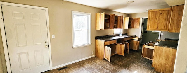 kitchen with baseboards, dark countertops, a sink, and brown cabinetry