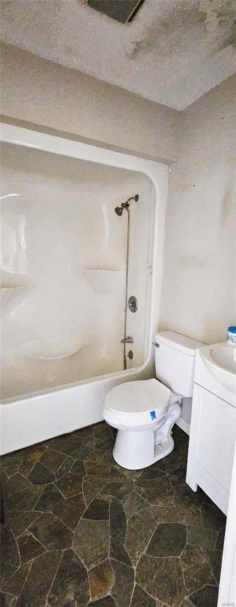 full bathroom with toilet, stone finish flooring, washtub / shower combination, and vanity