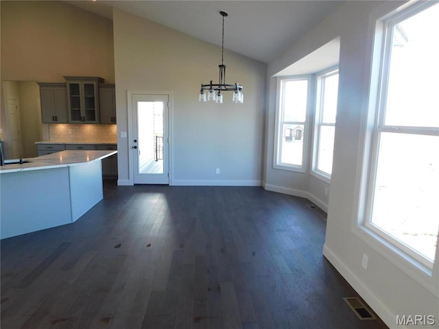 unfurnished dining area with a chandelier, dark wood finished floors, healthy amount of natural light, and high vaulted ceiling