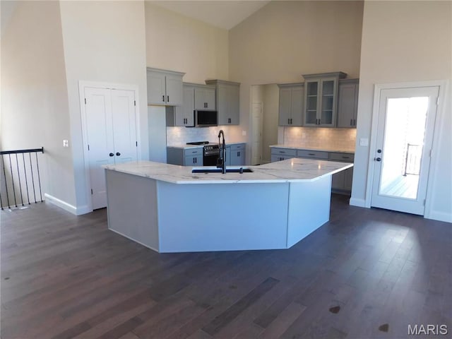 kitchen featuring a sink, high vaulted ceiling, gray cabinetry, a large island with sink, and tasteful backsplash
