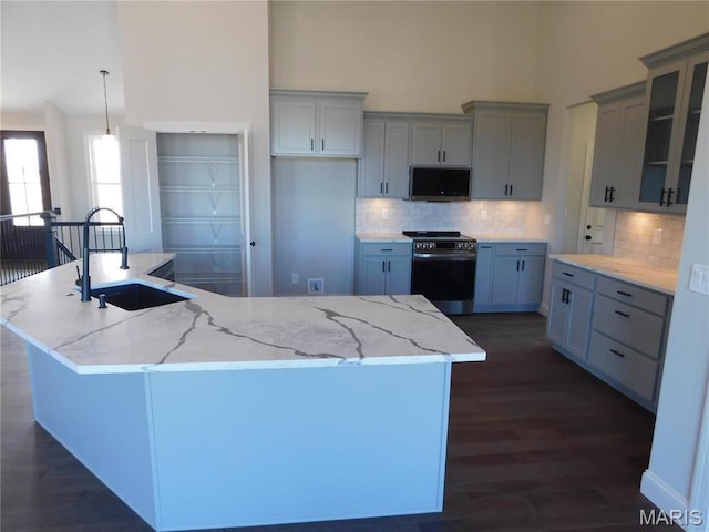 kitchen with electric range oven, a sink, a towering ceiling, dark wood-style floors, and backsplash