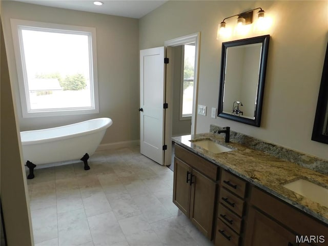 bathroom featuring healthy amount of natural light, a freestanding bath, double vanity, baseboards, and recessed lighting