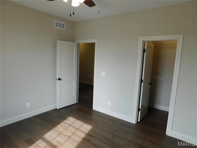 unfurnished bedroom featuring dark wood-style floors, baseboards, a spacious closet, a ceiling fan, and a closet