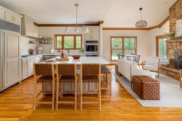 kitchen featuring custom range hood, stainless steel appliances, ornamental molding, light wood-type flooring, and a kitchen bar