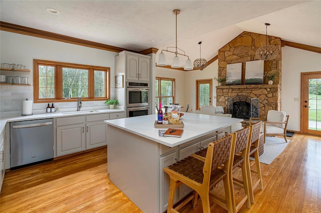 kitchen featuring appliances with stainless steel finishes, a sink, a kitchen bar, light wood-style flooring, and vaulted ceiling