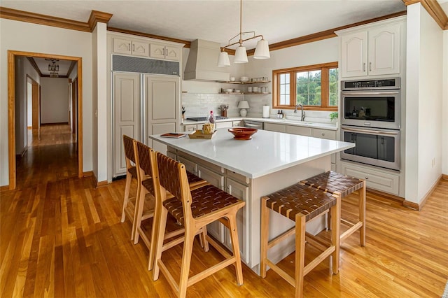 kitchen with stainless steel appliances, custom exhaust hood, a sink, a kitchen bar, and crown molding