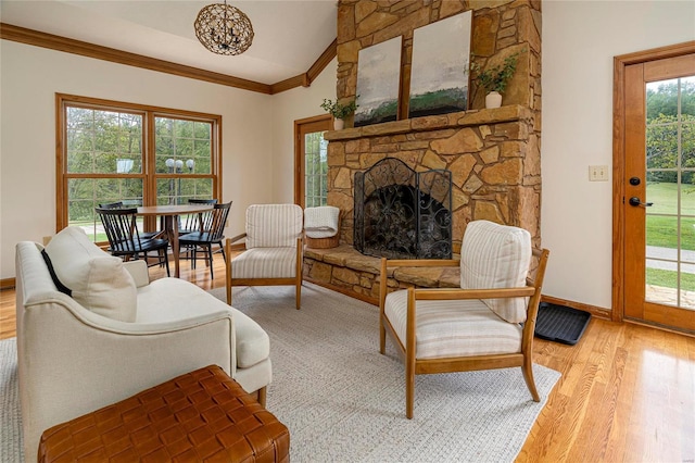 living area featuring light wood finished floors, ornamental molding, lofted ceiling, a stone fireplace, and baseboards