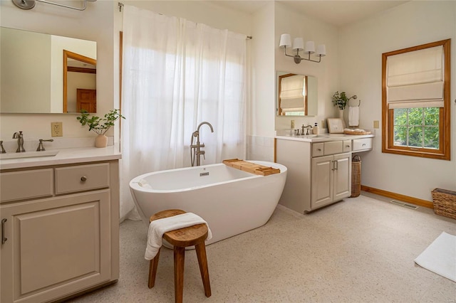 bathroom with a freestanding bath, two vanities, and baseboards
