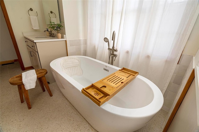 full bathroom with a soaking tub, vanity, and tile walls