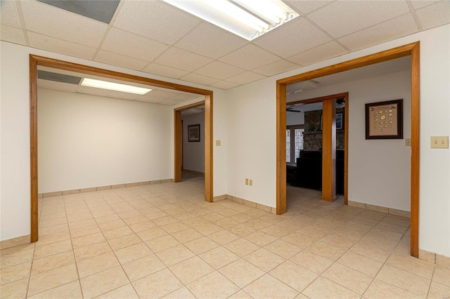 spare room featuring a drop ceiling, light tile patterned flooring, and baseboards