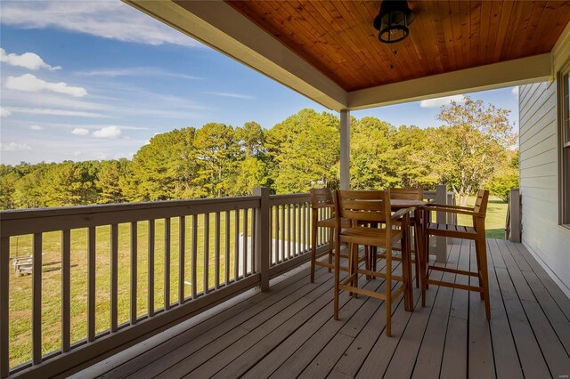 wooden terrace with a lawn, outdoor dining area, and a wooded view