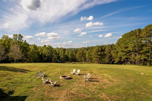 view of grassy yard featuring a fire pit and a wooded view