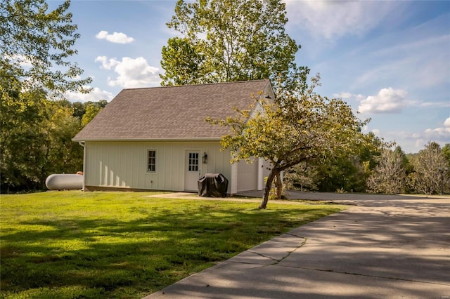 back of property featuring a lawn, a shingled roof, an outdoor structure, and concrete driveway