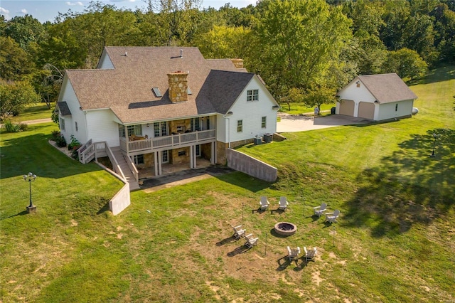 rear view of property with a fire pit, an outbuilding, a wooden deck, a yard, and a forest view