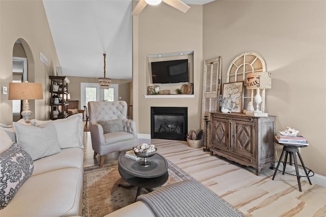 living room with wood finished floors, high vaulted ceiling, baseboards, a glass covered fireplace, and a ceiling fan