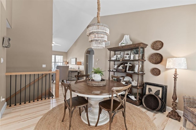 dining room with wood finished floors, a chandelier, arched walkways, baseboards, and high vaulted ceiling