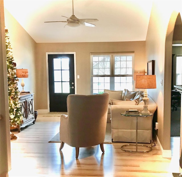 living room featuring vaulted ceiling, wood finished floors, ceiling fan, arched walkways, and baseboards