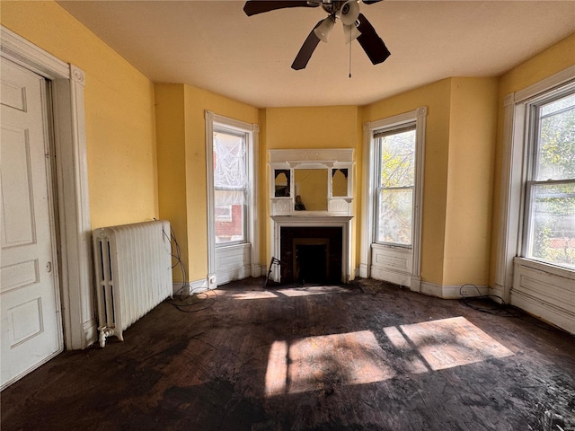 5168 Vernon Ave, Saint Louis, MO 63113 - unfurnished living room featuring radiator heating unit, a fireplace with flush hearth, a ceiling fan, and baseboards