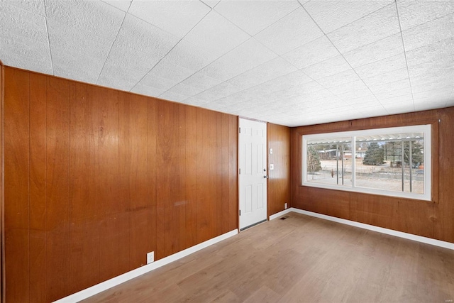 spare room featuring wood finished floors, wood walls, and baseboards