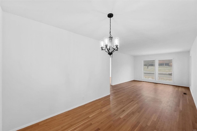 unfurnished dining area with a chandelier, wood finished floors, and baseboards
