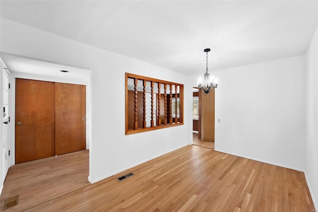 spare room with a chandelier, light wood-style floors, and baseboards