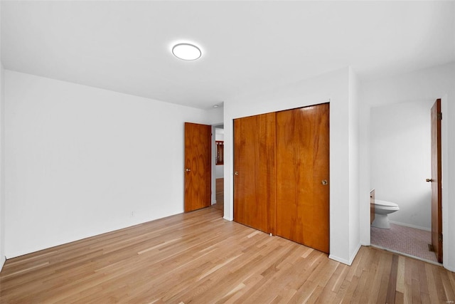 unfurnished bedroom featuring light wood-type flooring, a closet, and ensuite bath
