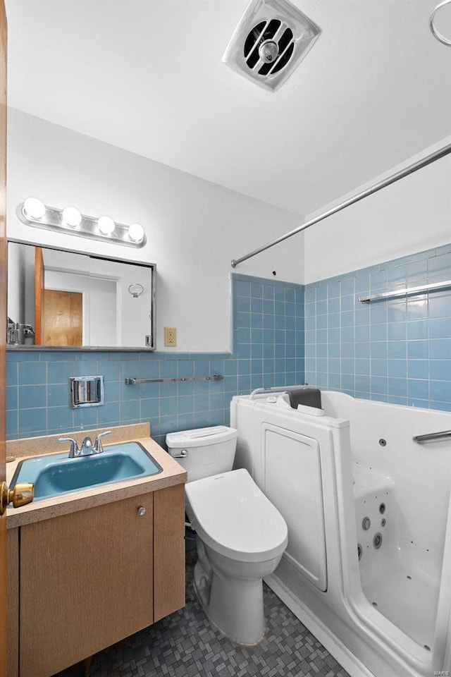bathroom featuring tile walls, toilet, a jetted tub, tile patterned flooring, and vanity