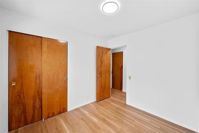 unfurnished bedroom featuring light wood-style flooring, a closet, and baseboards