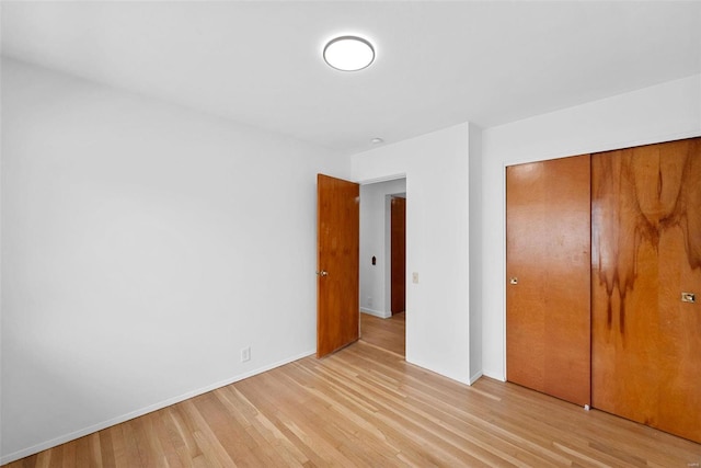unfurnished bedroom with light wood-type flooring, a closet, and baseboards