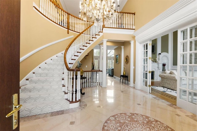entryway with french doors, a high ceiling, stairway, decorative columns, and a chandelier