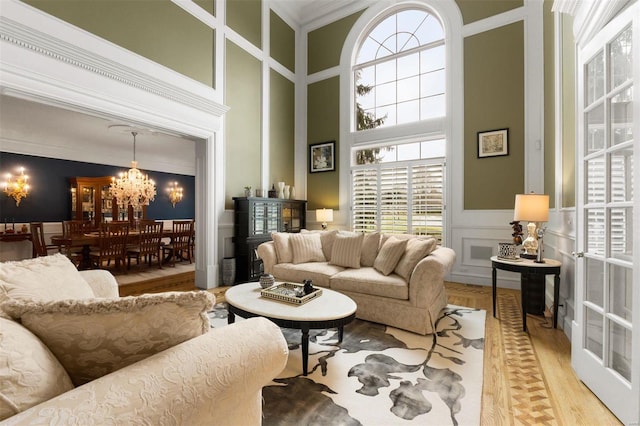 living area with a decorative wall, a towering ceiling, a chandelier, plenty of natural light, and light wood finished floors
