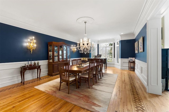 dining room with a chandelier, crown molding, a decorative wall, light wood-type flooring, and a wainscoted wall