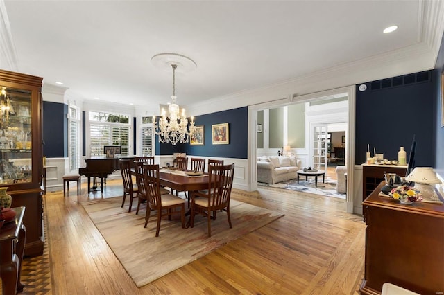 dining area featuring crown molding, light wood-style flooring, a chandelier, a decorative wall, and a wainscoted wall