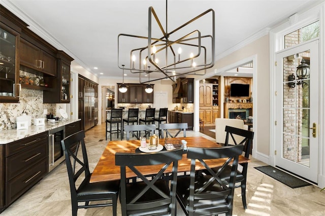 dining space with crown molding, a chandelier, recessed lighting, wine cooler, and a fireplace