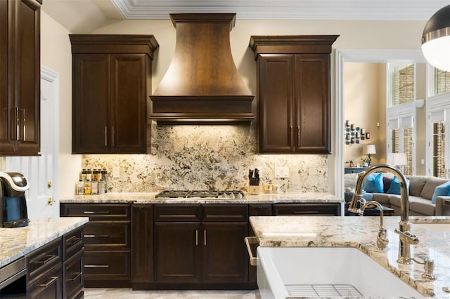 kitchen featuring premium range hood, a sink, stainless steel gas stovetop, light stone countertops, and dark brown cabinetry