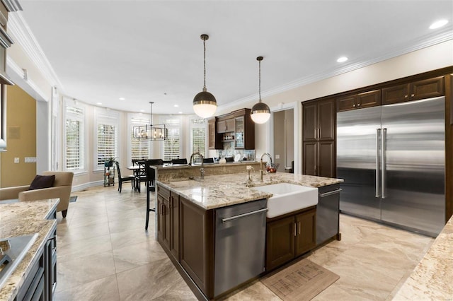kitchen with appliances with stainless steel finishes, a sink, dark brown cabinetry, ornamental molding, and a center island with sink