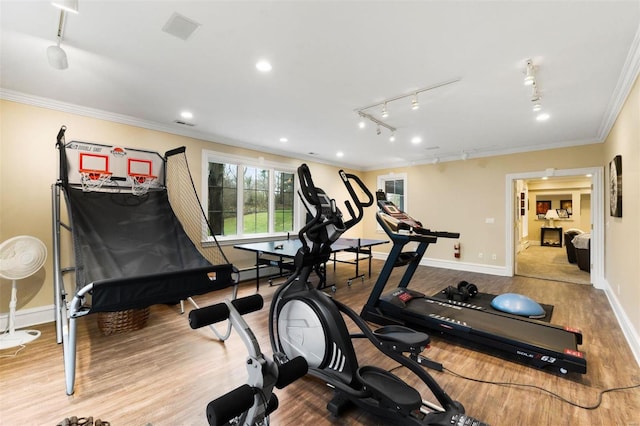 exercise area with ornamental molding, rail lighting, wood finished floors, and baseboards