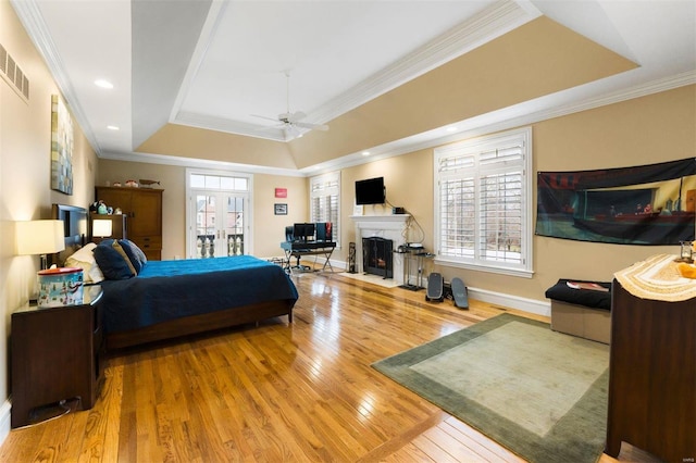 bedroom featuring wood finished floors, french doors, a tray ceiling, crown molding, and baseboards