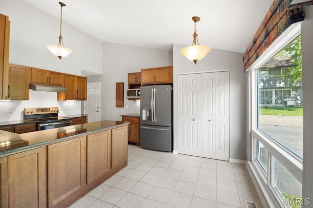 kitchen with appliances with stainless steel finishes, light tile patterned floors, brown cabinetry, hanging light fixtures, and under cabinet range hood