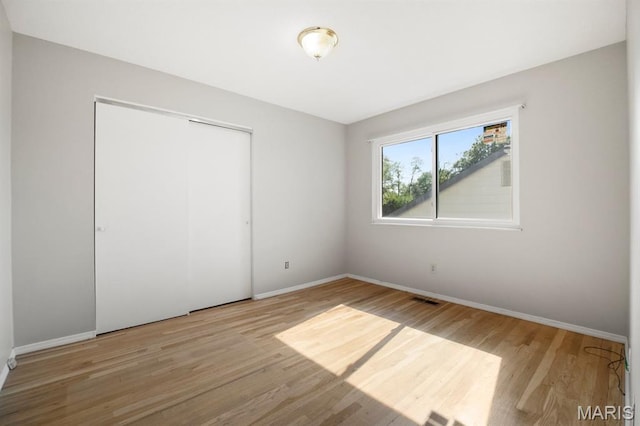 unfurnished bedroom featuring wood finished floors, baseboards, and a closet