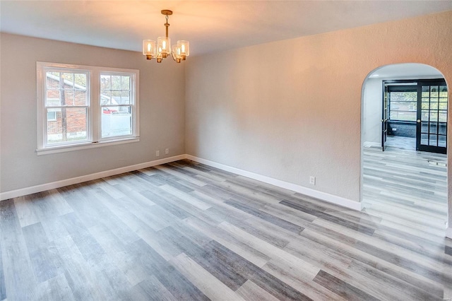 empty room featuring arched walkways, healthy amount of natural light, and wood finished floors