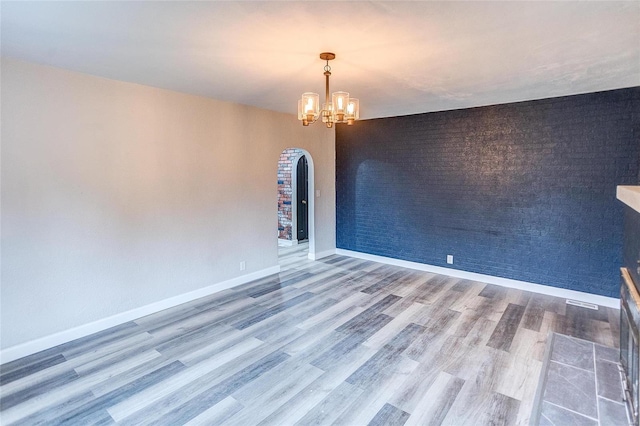 empty room featuring arched walkways, a chandelier, wood finished floors, and baseboards
