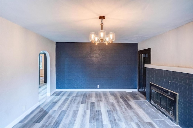 unfurnished living room with a chandelier, wood finished floors, a fireplace with flush hearth, arched walkways, and baseboards