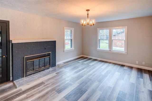 unfurnished living room featuring a chandelier, wood finished floors, a brick fireplace, and baseboards