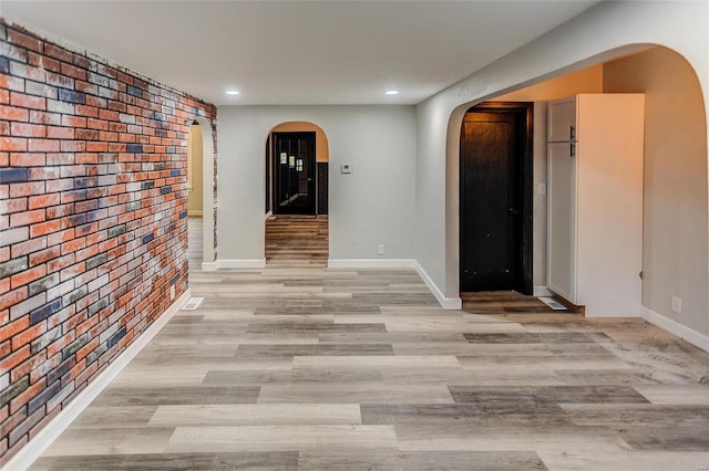 corridor featuring arched walkways, brick wall, light wood-type flooring, recessed lighting, and baseboards