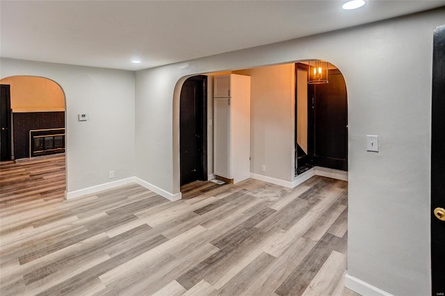 empty room with arched walkways, recessed lighting, light wood-type flooring, and baseboards