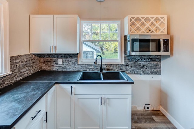 kitchen with stainless steel microwave, a sink, dark countertops, backsplash, and white cabinets