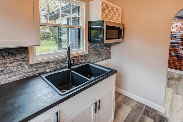 kitchen featuring a sink, stainless steel microwave, dark countertops, wood finished floors, and backsplash