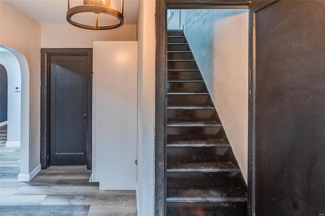 stairs with arched walkways, wood finished floors, and baseboards