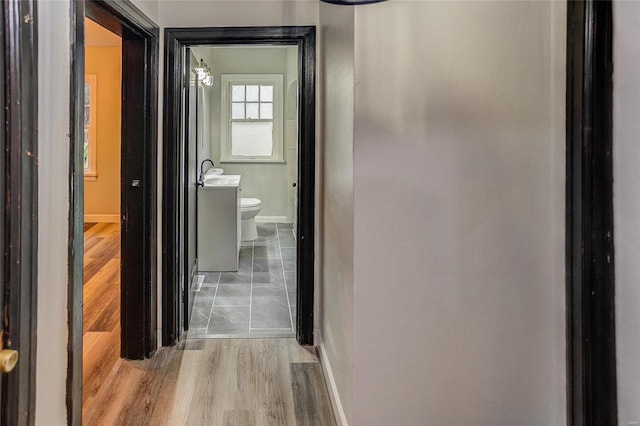 hall with baseboards, wood finished floors, and a sink